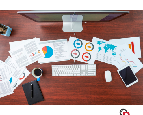 Several pages of a media monitoring report spread out across a work desk with a computer on it.